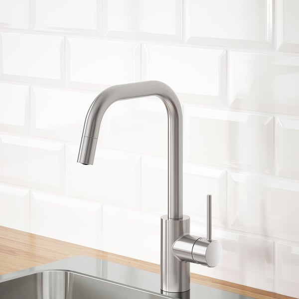 Modern kitchen faucet with pull-out spout, stainless steel finish, mounted on wood countertop against white subway tile backdrop.