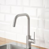 Modern kitchen faucet with pull-out spout, stainless steel finish, mounted on wood countertop against white subway tile backdrop.