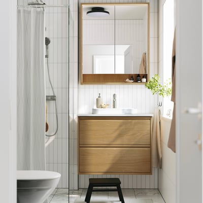 Modern bathroom with wooden vanity, white sink, and mirror. Toiletries on shelf, shower, and bathtub.