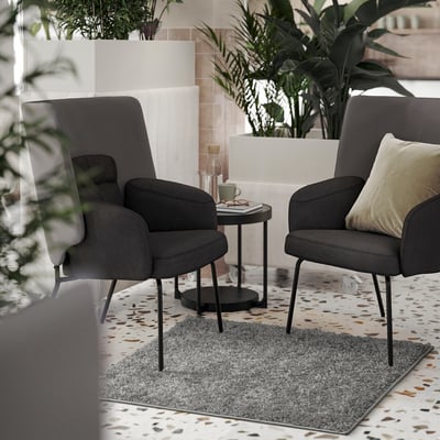 Dark grey armchairs, large light grey shaggy rug, side table with mug and book.