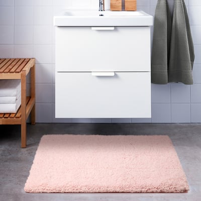 Modern bathroom with white vanity, light pink rectangular bath mat, grey towels.