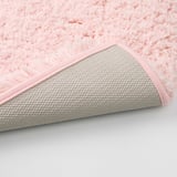 Close-up of a soft, pink, plush bath mat with a textured, non-slip base.