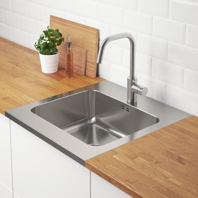 Stainless steel kitchen sink with a faucet, set in wooden countertop. Plant and oil bottle sit on the counter.