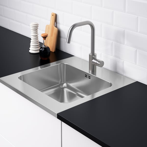 Stainless steel sink with single lever faucet, set in dark countertop, backed by white tiles.