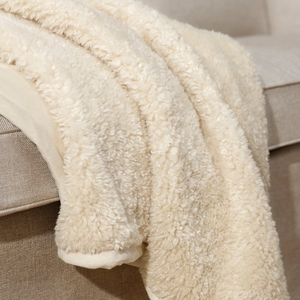A plush, cream-colored blanket draped over a bed, showcasing its soft, textured teddy bear-like material, inviting warmth and comfort.