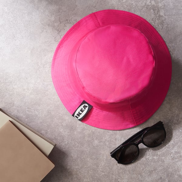Pink IKEA bucket hat on floor, book, sunglasses.