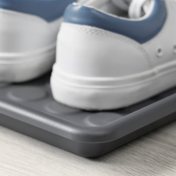 Close-up of a white and blue sneaker resting on a gray plastic shoe mat on a wooden floor.