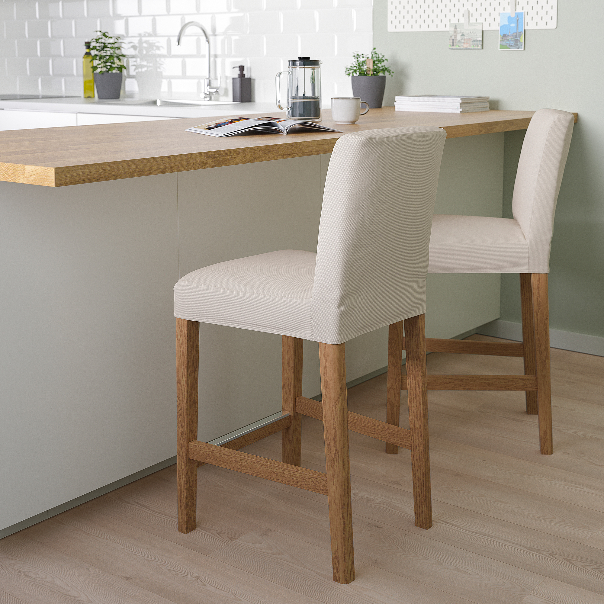 Two BERGMUND bar stools with beige covers and wooden legs beside kitchen island. Comfortable with backrest, in modern kitchen setting.