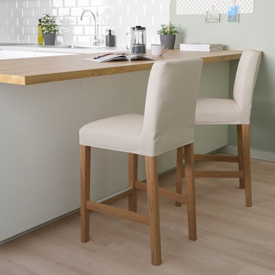 Two BERGMUND bar stools with beige covers and wooden legs beside kitchen island. Comfortable with backrest, in modern kitchen setting.