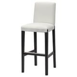 A white BERGMUND barstool with a black metal frame, featuring a padded seat and backrest for comfort.
