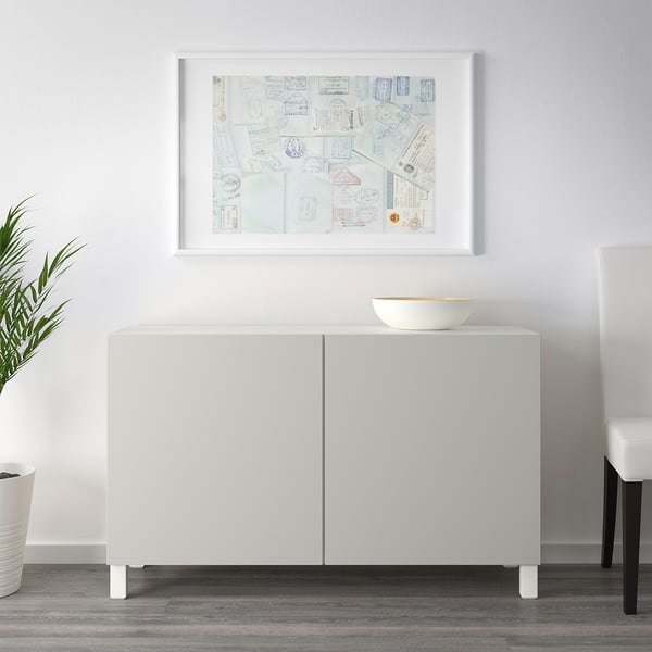 A white sideboard with two doors and a top surface holding a bowl. A framed art piece hangs above.