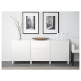 White storage unit with drawers and shelves, styled with decor items. Framed photos hang above.