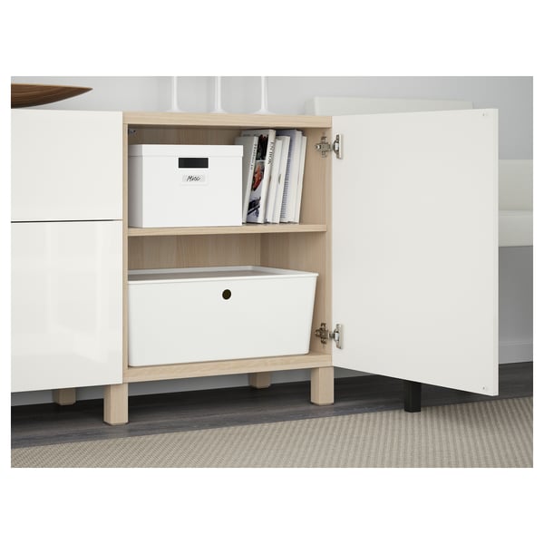White cabinet with wooden legs, showcasing adjustable shelves storing a labeled box, books, and a white container.