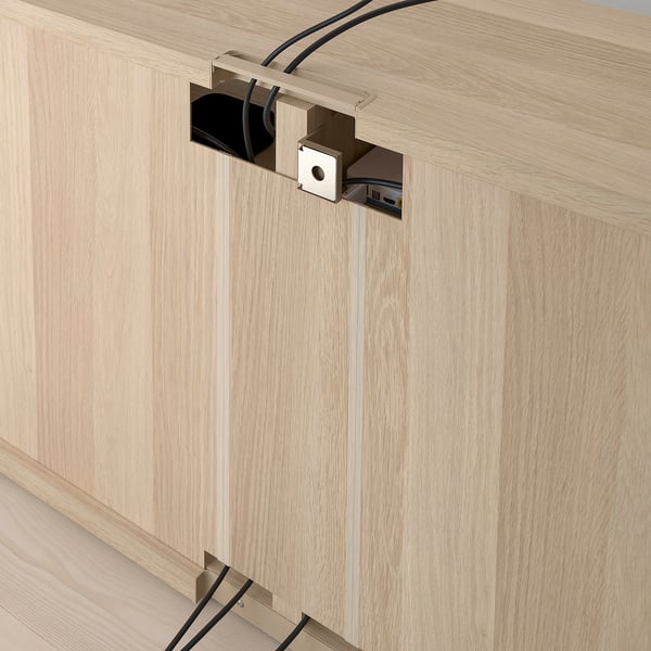 A BESTÅ tv bench with cable management. Cables are neatly organised through a built-in outlet in the light wood panelling.