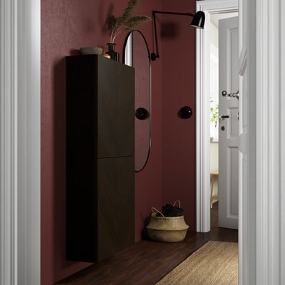 Dark wooden BESTÅ cabinet in small, styled entryway with burgundy walls, black handles, and round wall lamp.