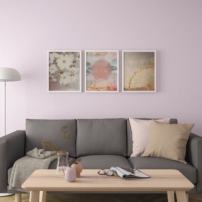 Modern living room with lilac walls, grey sofa, and three framed art prints above. Coffee table with candles and decor.