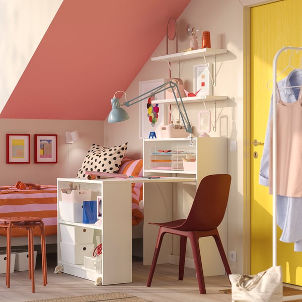 Bright room with BILLY desk, red chair, yellow door, and slanted ceiling. Desk has polka-dot cushion, shelves hold supplies.