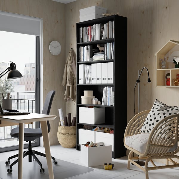 Black BILLY bookcase with books, boxes, desk, chair, wicker chair, clock.