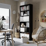 Black BILLY bookcase with books, boxes, desk, chair, wicker chair, clock.