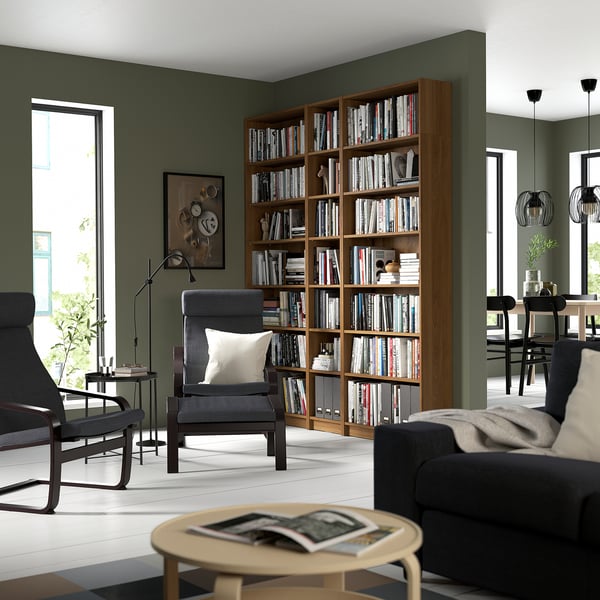Modern living room with tall BILLY bookcase filled with books, grey armchairs, wooden coffee table, and large windows.