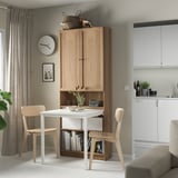 Modern dining area with light wood BILLY bookcase desk combo, white table, chairs, plant, and kitchen appliances.