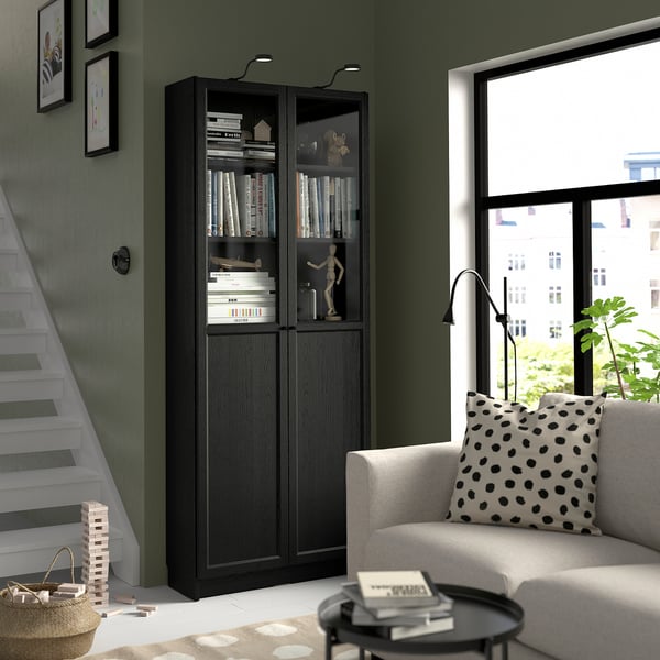 BILLY bookcase with books, decor, near stairs. Gray sofa, city view, lamp, plant.