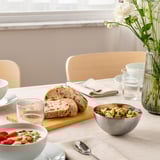 Breakfast table with cereal, bread, nuts, and flowers.