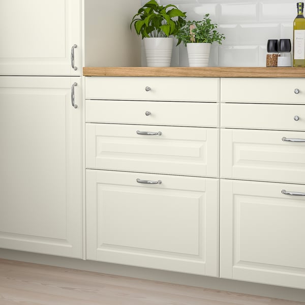 White BODBYN kitchen drawers, smooth lacquered off-white, traditional bevelled panels, compact size, storage beneath green plants.