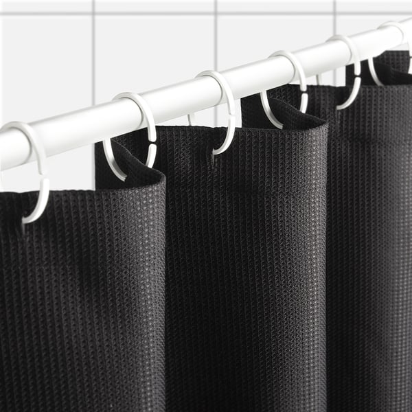 Black shower curtain with waffle texture hangs from white rod using plastic hooks, demonstrating its water-repellent and durable design.