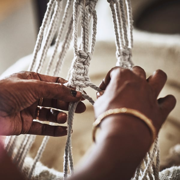 Person crafting with gray cotton strings, wearing rings and bracelet.