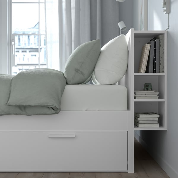 A BRIMNES bed frame featuring hidden storage drawers and a headboard with built-in shelves for books and items, ideal for small spaces.