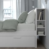 A BRIMNES bed frame featuring hidden storage drawers and a headboard with built-in shelves for books and items, ideal for small spaces.