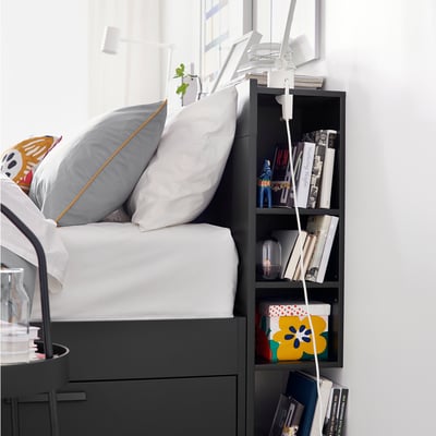 Black BRIMNES bed with grey pillows, books, and a lamp on the headboard, showcasing a cozy bedroom setup.