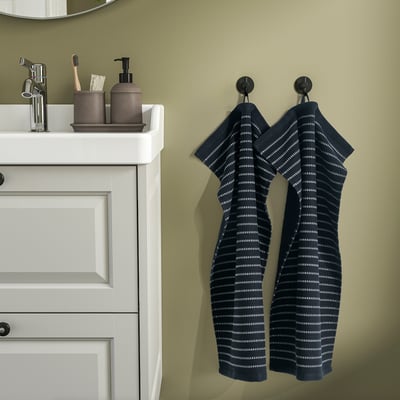 Two blue towels hang on black hooks; white cabinet with silver faucet.
