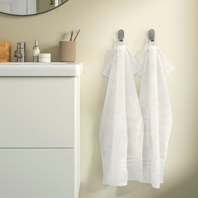Two white towels hang on hooks beside a white vanity with toiletries. A mirror reflects part of the room.