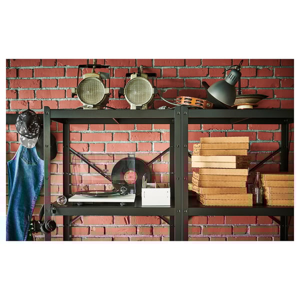 Black storage unit with shelves against a red brick wall. It holds a record player, books, and vintage lamps.