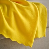 Bright yellow fleece throw draped on a gray surface, showcasing soft texture and quality.