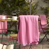Pink fleece blanket DAGGKÅPOR draped on chair, larger than cups & plates on table.
