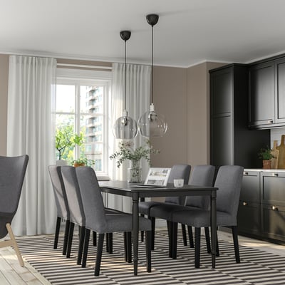 Modern dining room with black table, grey chairs, large window, pendant lights, dark cabinets, striped rug, recycled polyester chair covers.