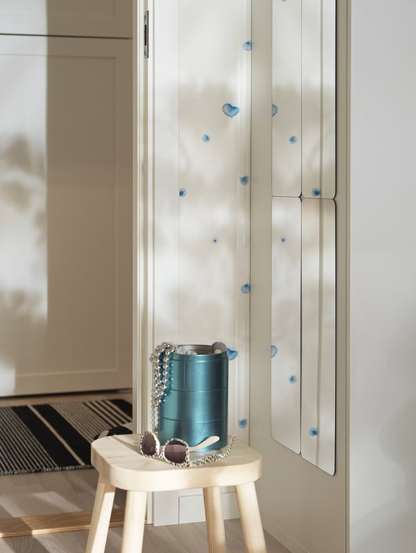 Small white stool with blue vase and accessories. Behind it, a tall wardrobe mirror with blue decals.