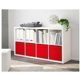 A white bookshelf with red drawers, holding records, books, and a plant.