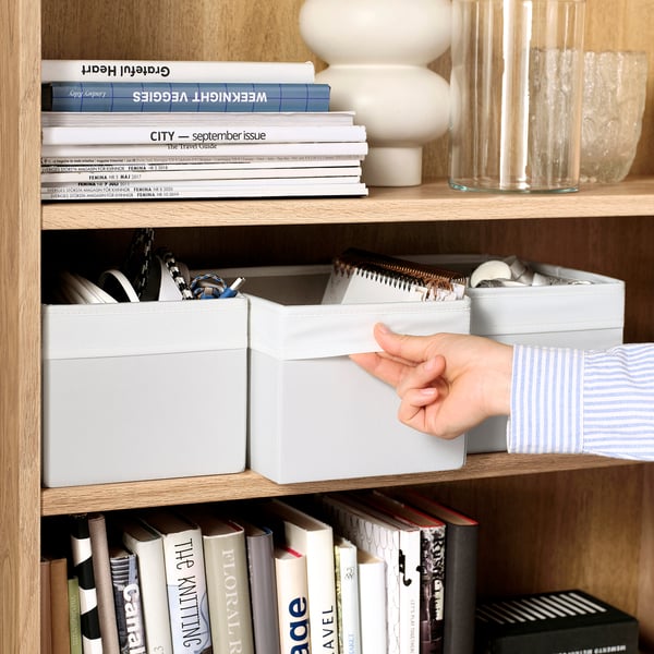 A person pulling out a white fabric storage box from a wooden shelf, demonstrating its function in organising and accessing items easily.