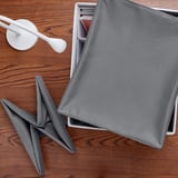 Foldable fabric lid protecting items in box on wooden table. Two grey napkins are visible, one folded in star shape and another in rectangle form.