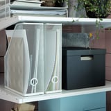 White metal mesh magazine holders with colorful accents, a gray box, and small plant on a white shelf.