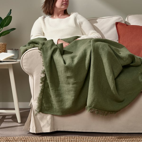 Woman draped in green throw blanket on sofa, reading.