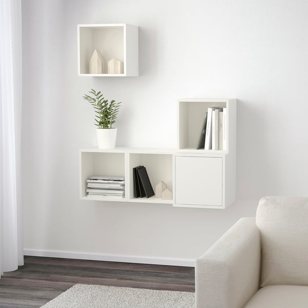 Minimalist white wall-mounted shelf unit. Three compartments hold books, a plant, and decor. Efficient storage solution.