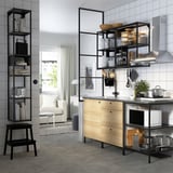 Modern kitchen with wooden cabinets and open shelves, stainless steel appliances, glassware, cutlery, and black metal accents.