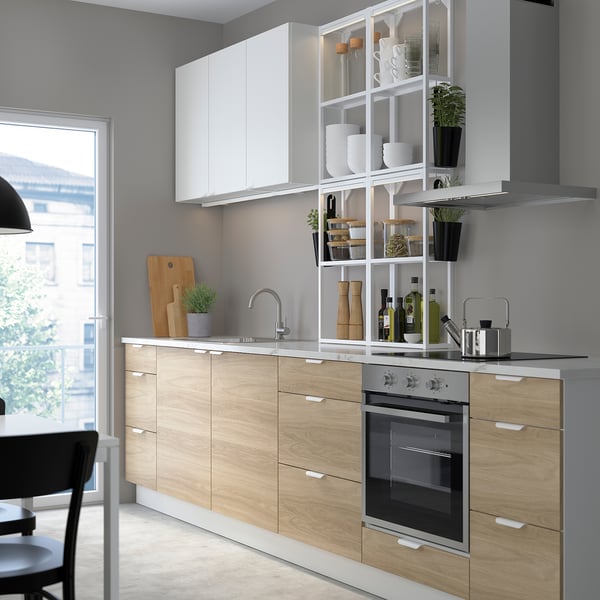 Modern kitchen with light wood cabinets, white shelves, stainless steel appliances, and a large window.