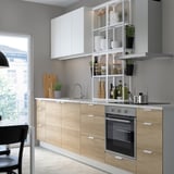 Modern kitchen with light wood cabinets, white shelves, stainless steel appliances, and a large window.