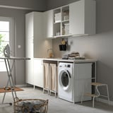 Modern laundry room with white ENHET cabinets. Washing machine, sink, and ironing board. Linen and cleaning supplies neatly stored.